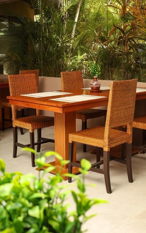 Mesa de jantar para pátio externo com quatro cadeiras de vime rodeadas por vegetação exuberante.