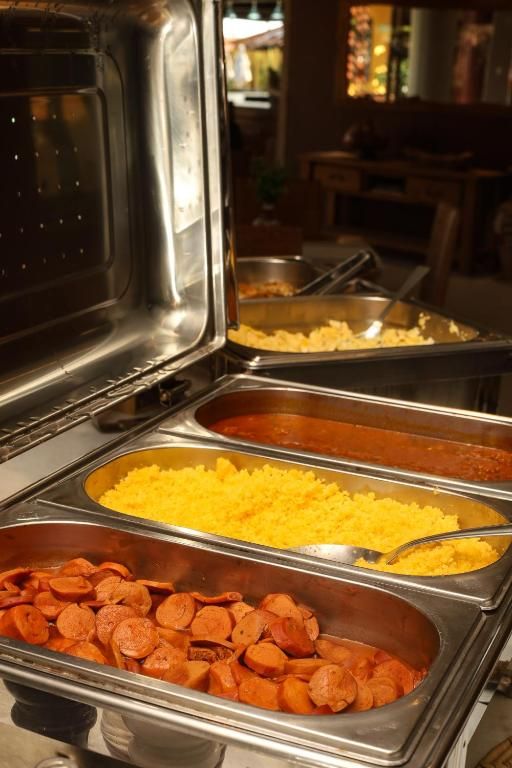 Bandejas de buffet com fatias de pepperoni, ovos mexidos e um rechaud de prata em uma área de refeições.
