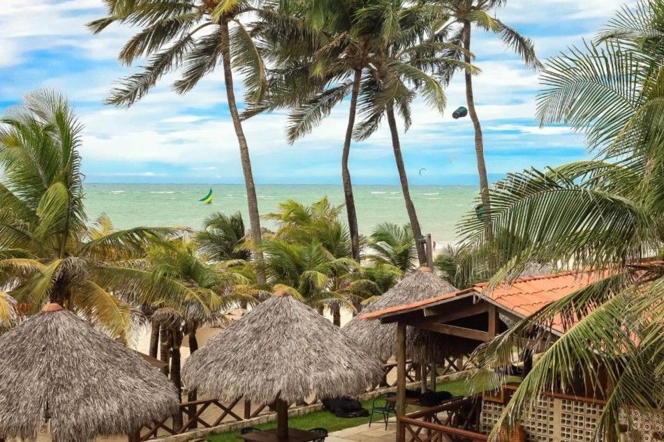Resort tropical à beira-mar com palmeiras, cabanas de palha e um oceano azul-turquesa ao fundo.