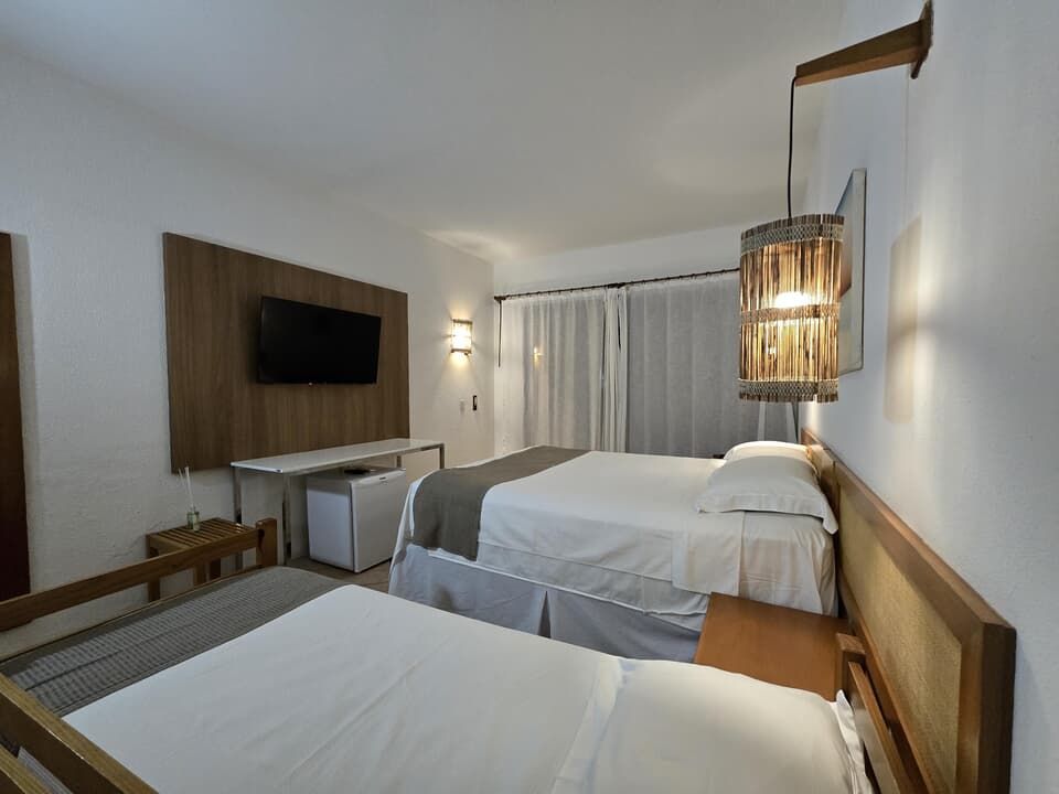 Quarto moderno com duas camas, TV de parede, detalhes em madeira e iluminação suave.