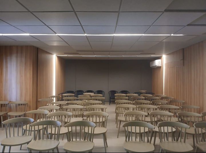 Sala de conferências vazia com fileiras de cadeiras voltadas para um palco e uma tela de projeção.