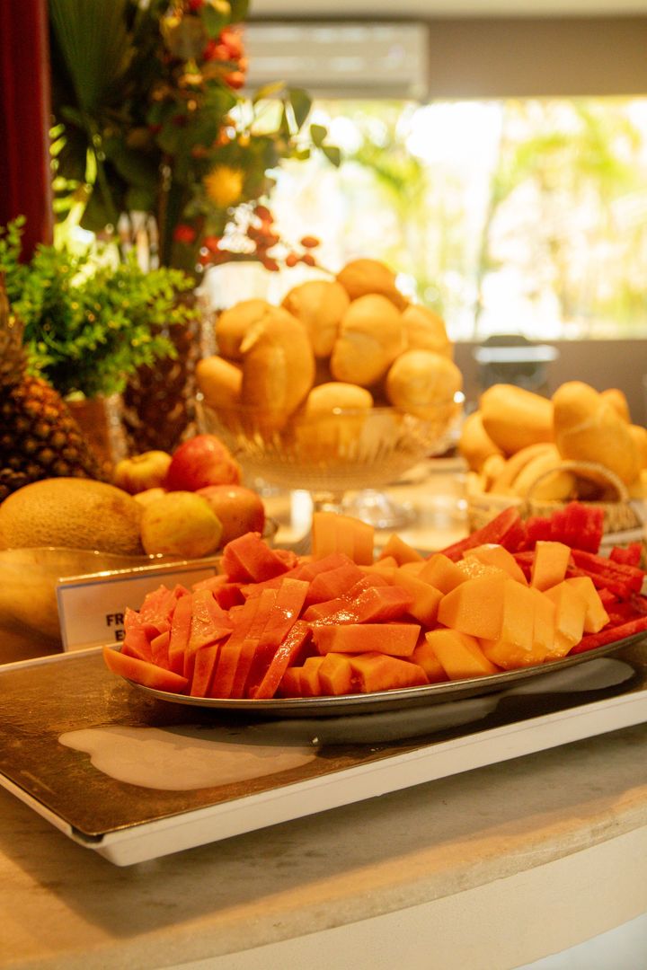 Prato de frutas com fatias de melão e melancia em uma mesa de buffet bem iluminada.