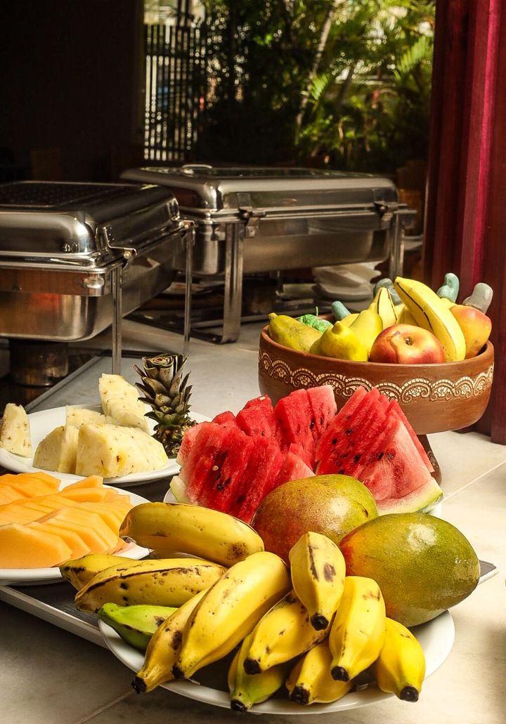 Frutas tropicais frescas variadas, dispostas em travessas e em uma cesta sobre uma mesa de bufê.