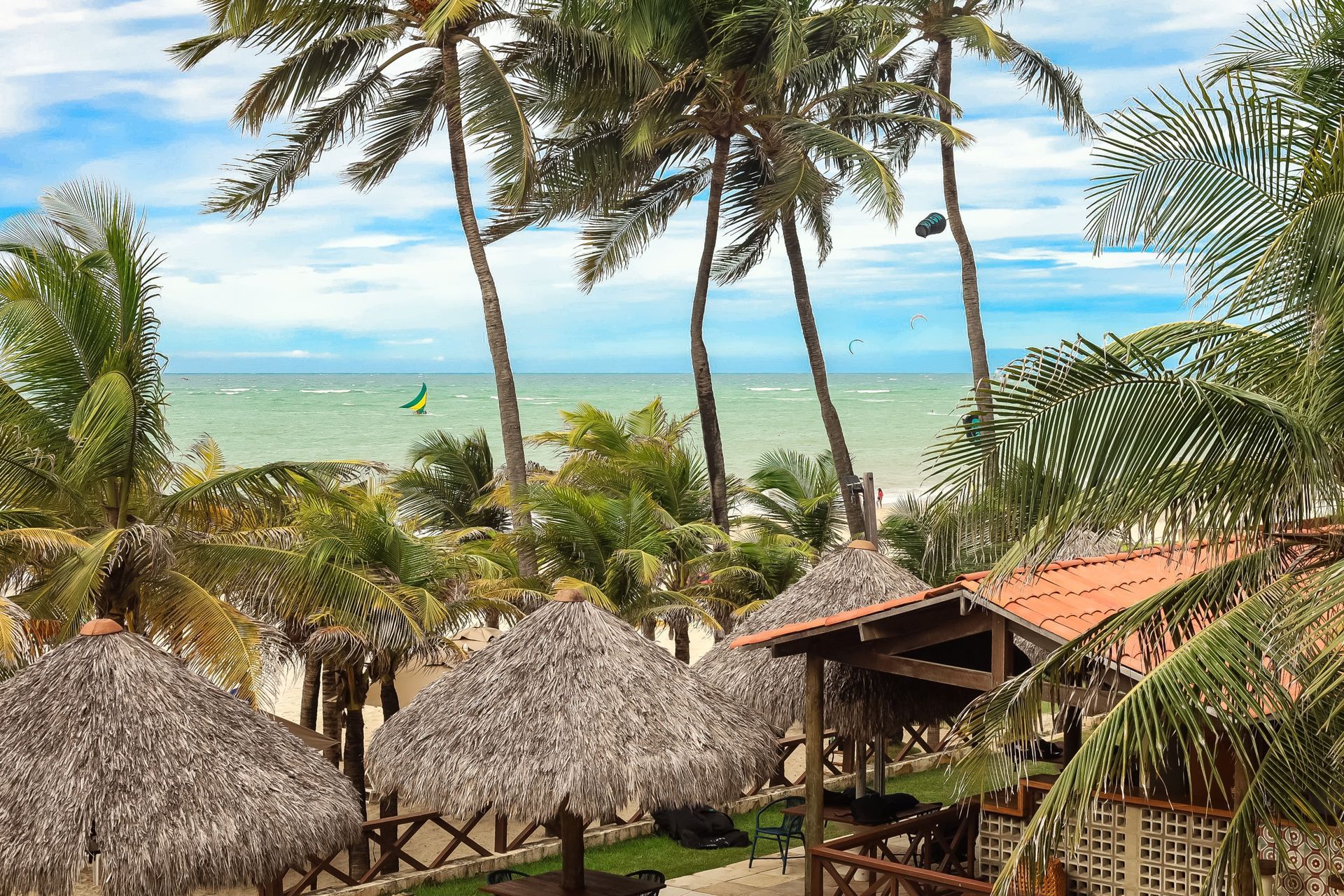 Resort tropical à beira-mar com palmeiras, cabanas de palha e oceano turquesa sob um céu claro.