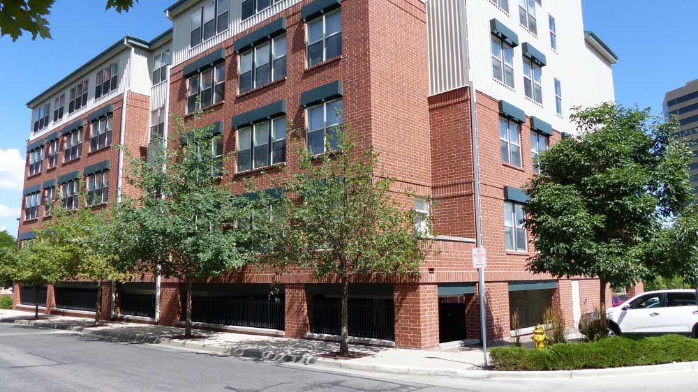 Modern brick-and-white apartment building with street-level parking and trees on a city corner