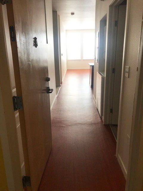 Narrow hallway with wooden floor, open doors, and bright light at the far end.