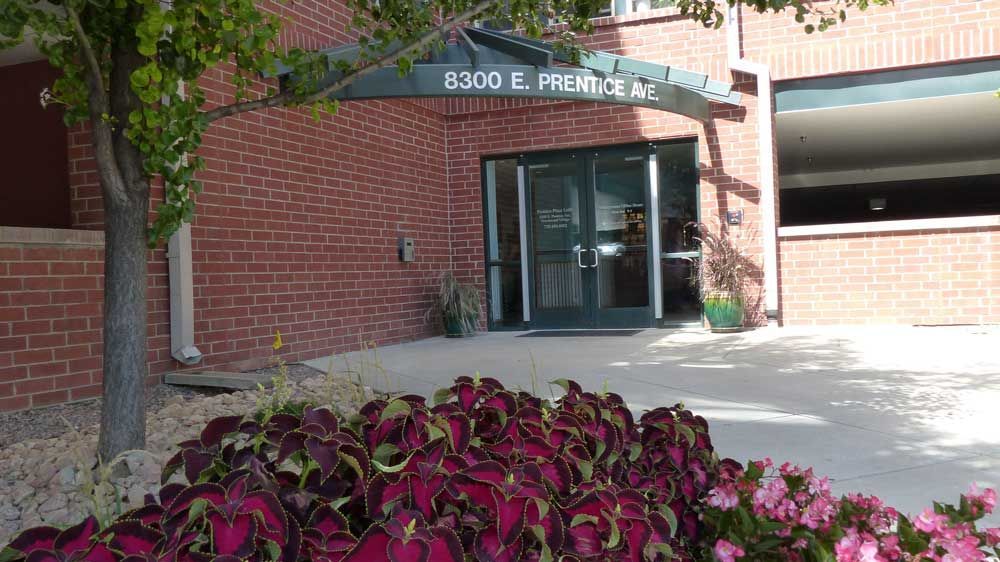 Brick building entrance with glass doors, green awning, and flower bed in front
