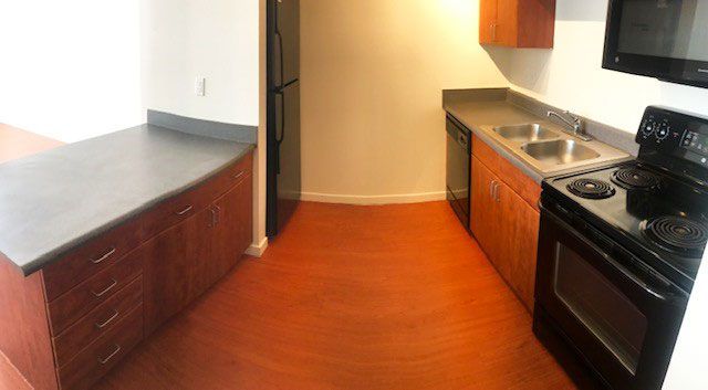 Compact kitchen with wood floors, dark cabinets, black appliances, and a stainless sink and fridge
