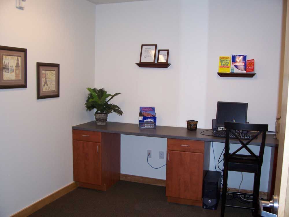 Small office corner with desk, computer, plant, shelves, and framed wall art