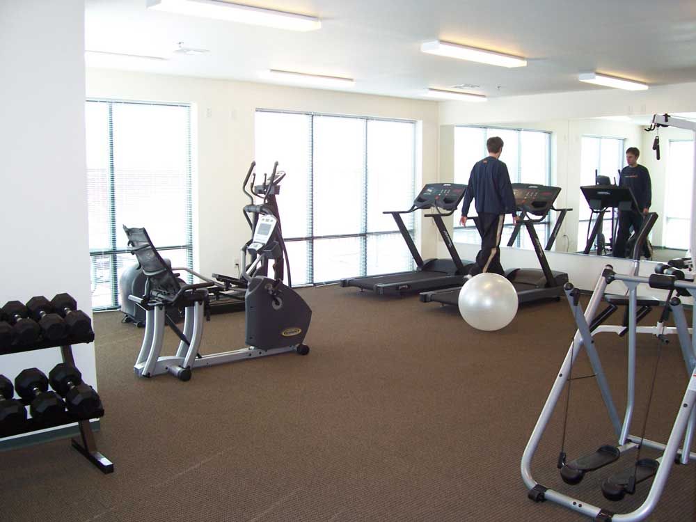 Fitness room with treadmills, weights, and exercise machines, with two people using treadmills.