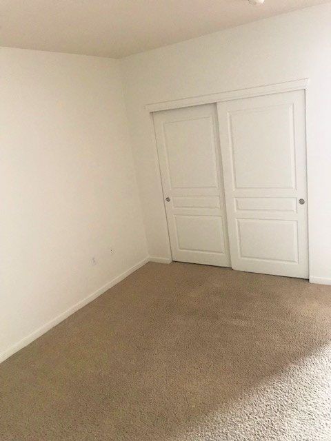 Empty beige-carpeted room with white walls and double white closet doors
