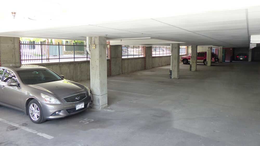 Covered parking garage with a silver car and concrete pillars, viewed from inside.
