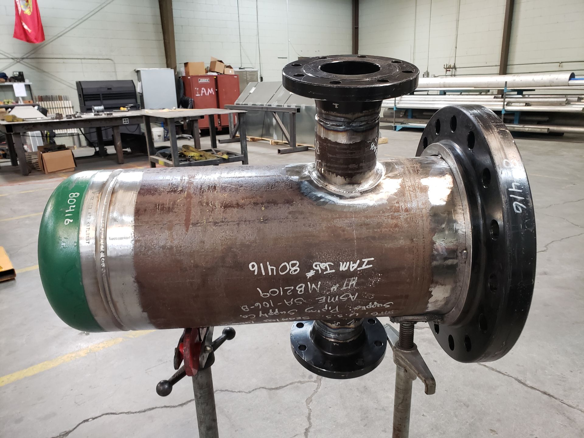 Welded industrial pipe assembly with flanges and a threaded fitting. Green cap, brown steel, black flanges.