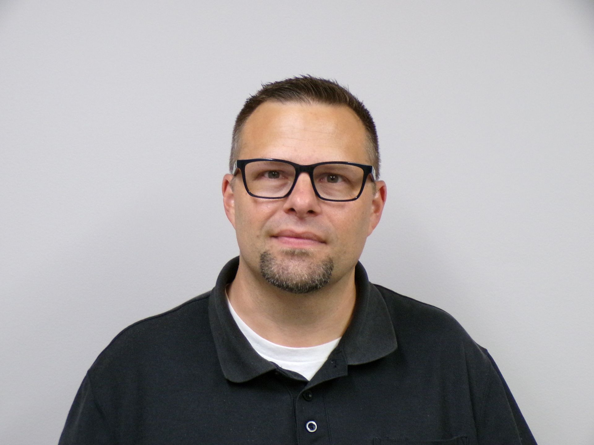 Man in blue collared shirt with IAM logo, smiling in front of a neutral backdrop.