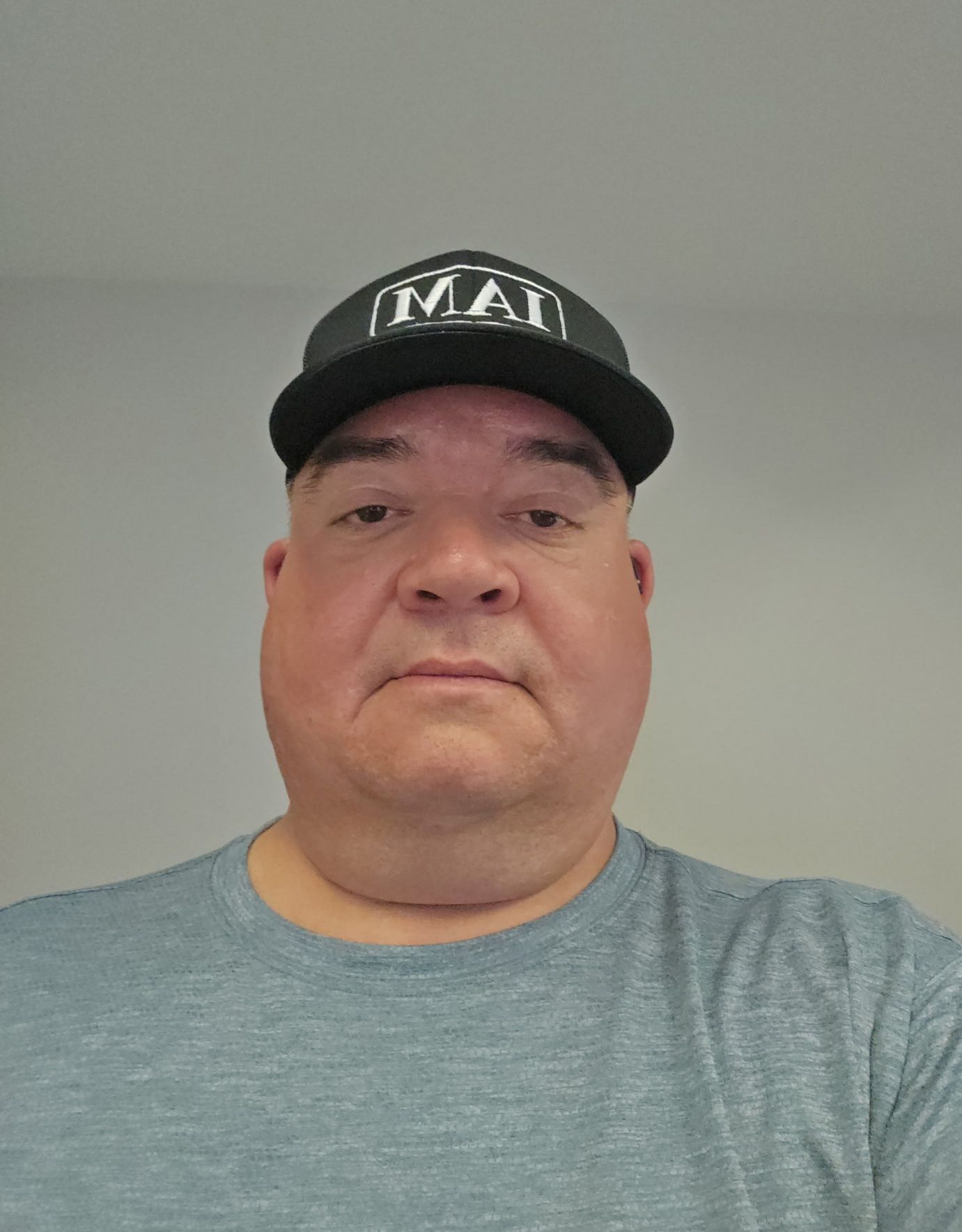 Man in blue collared shirt with IAM logo, smiling in front of a neutral backdrop.