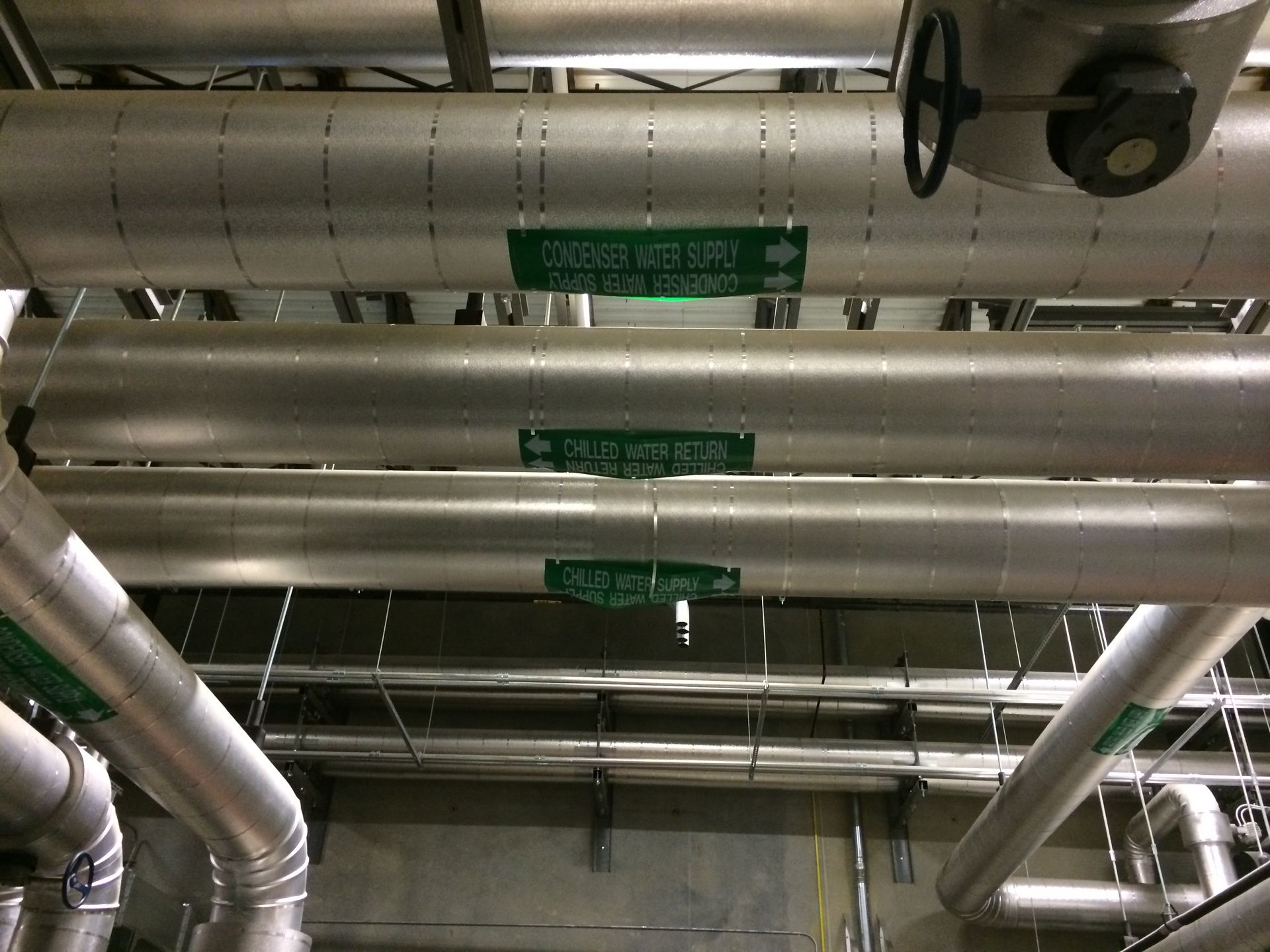 Pipes with green labels in a industrial setting. Labels indicate fluid directions.