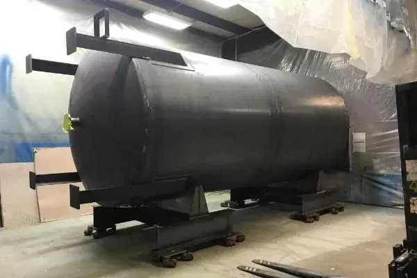 Large black cylindrical tank on a wheeled base, with support arms. In an industrial setting.