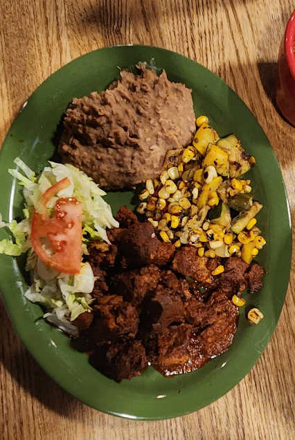 Plate of Mexican food: refried beans, corn, shredded meat, salad with tomato.
