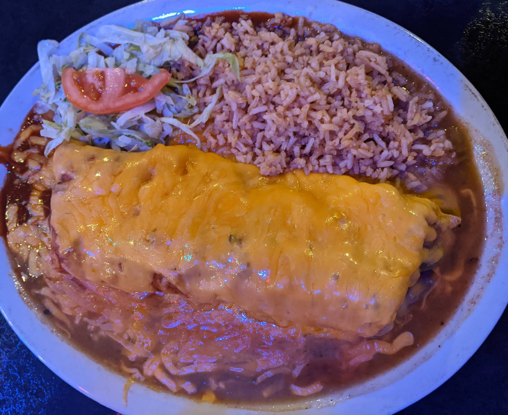 Burrito covered in melted cheese with rice, beans, lettuce, and tomato on a plate.