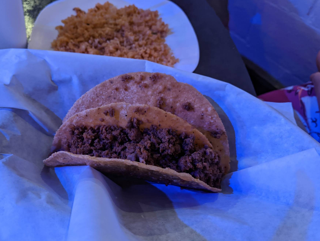 Two fried tacos with visible ground meat in a basket, rice in the background.