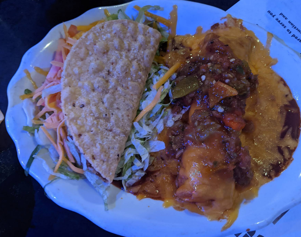 Taco and enchilada combo on a white plate, with shredded lettuce and cheese, and a red salsa sauce.