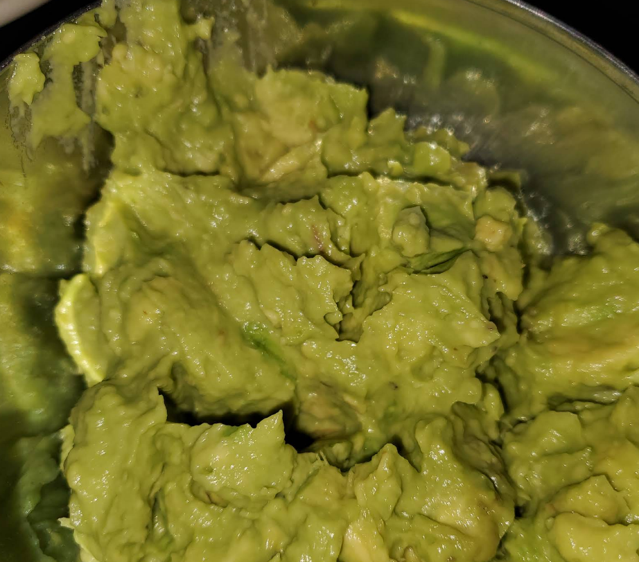 Close-up of mashed green avocado in a stainless steel bowl.