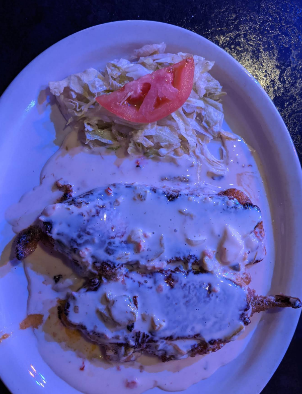 Two chile rellenos covered in cream sauce with a side of lettuce and tomato on a plate.