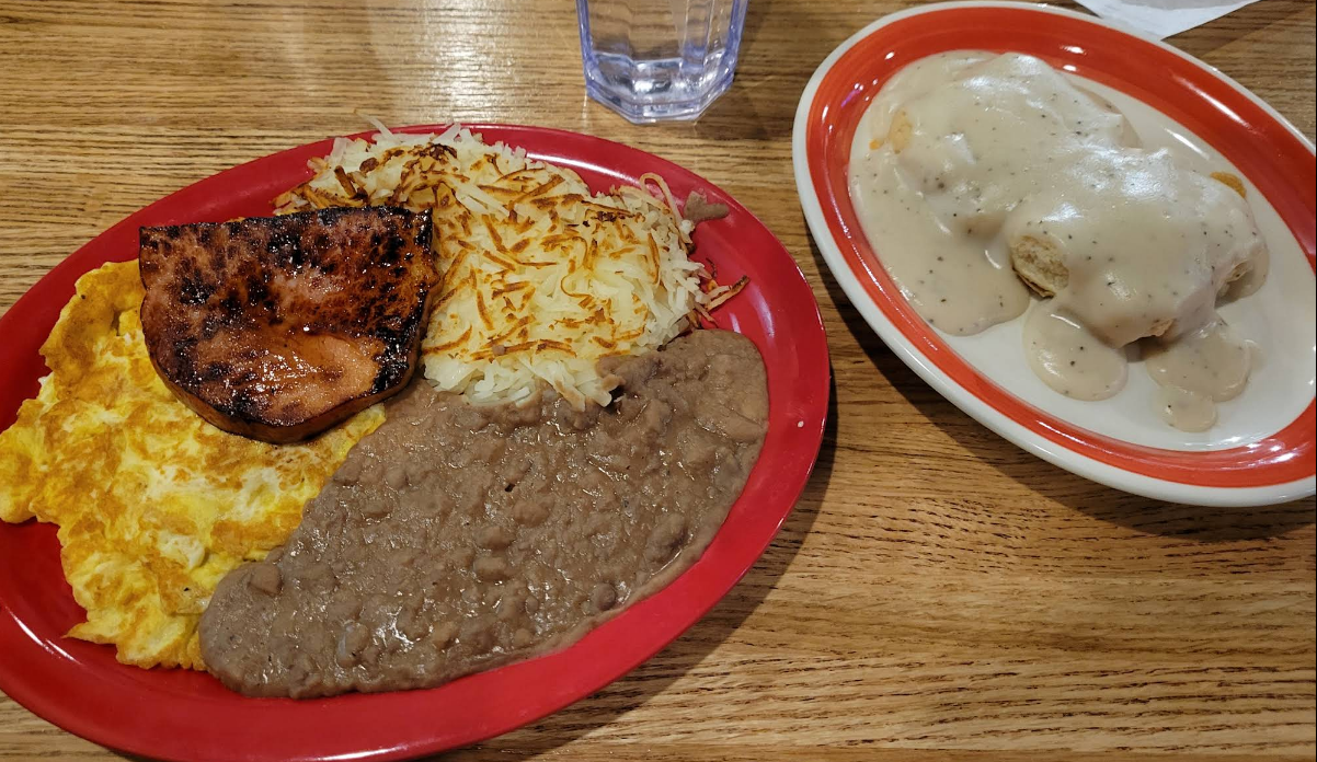 Breakfast plate with meat, eggs, hash browns, and biscuits with gravy; glass of water.