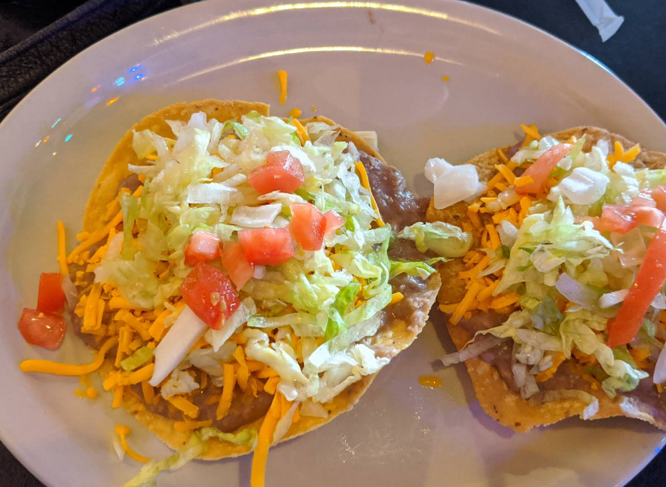 Two tostadas topped with beans, cheese, lettuce, and tomatoes on a white plate.