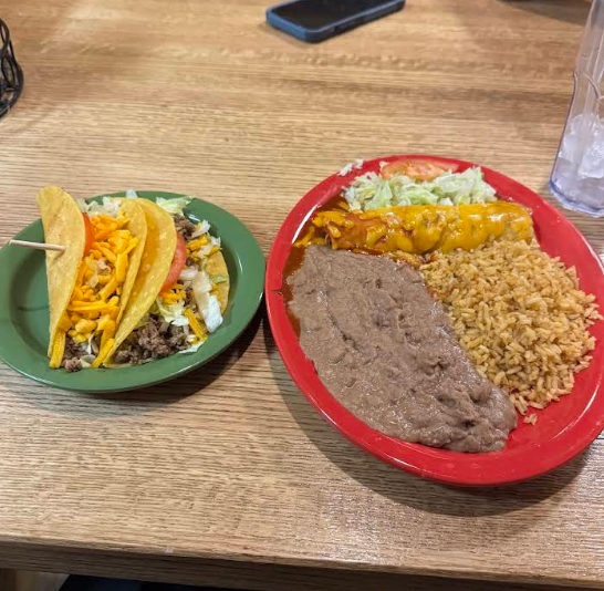 Tacos on a green plate, next to a red plate with enchilada, rice, and beans on a wooden table.