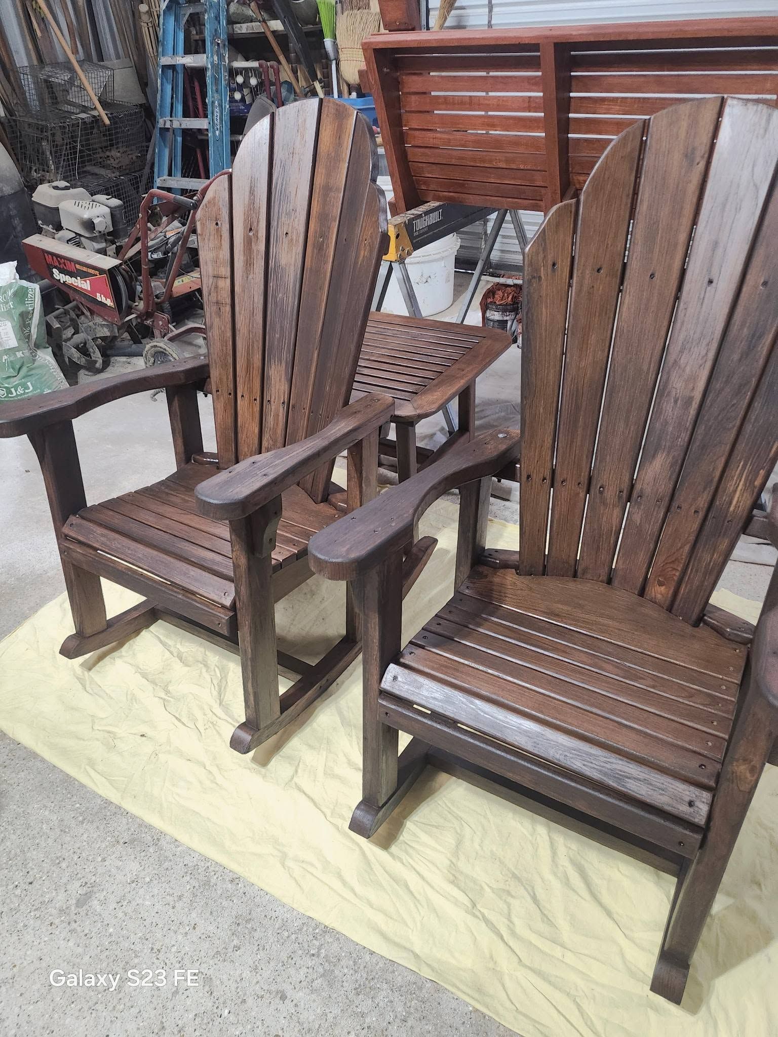Two wooden Adirondack chairs with slatted backs on a yellow tarp outdoors