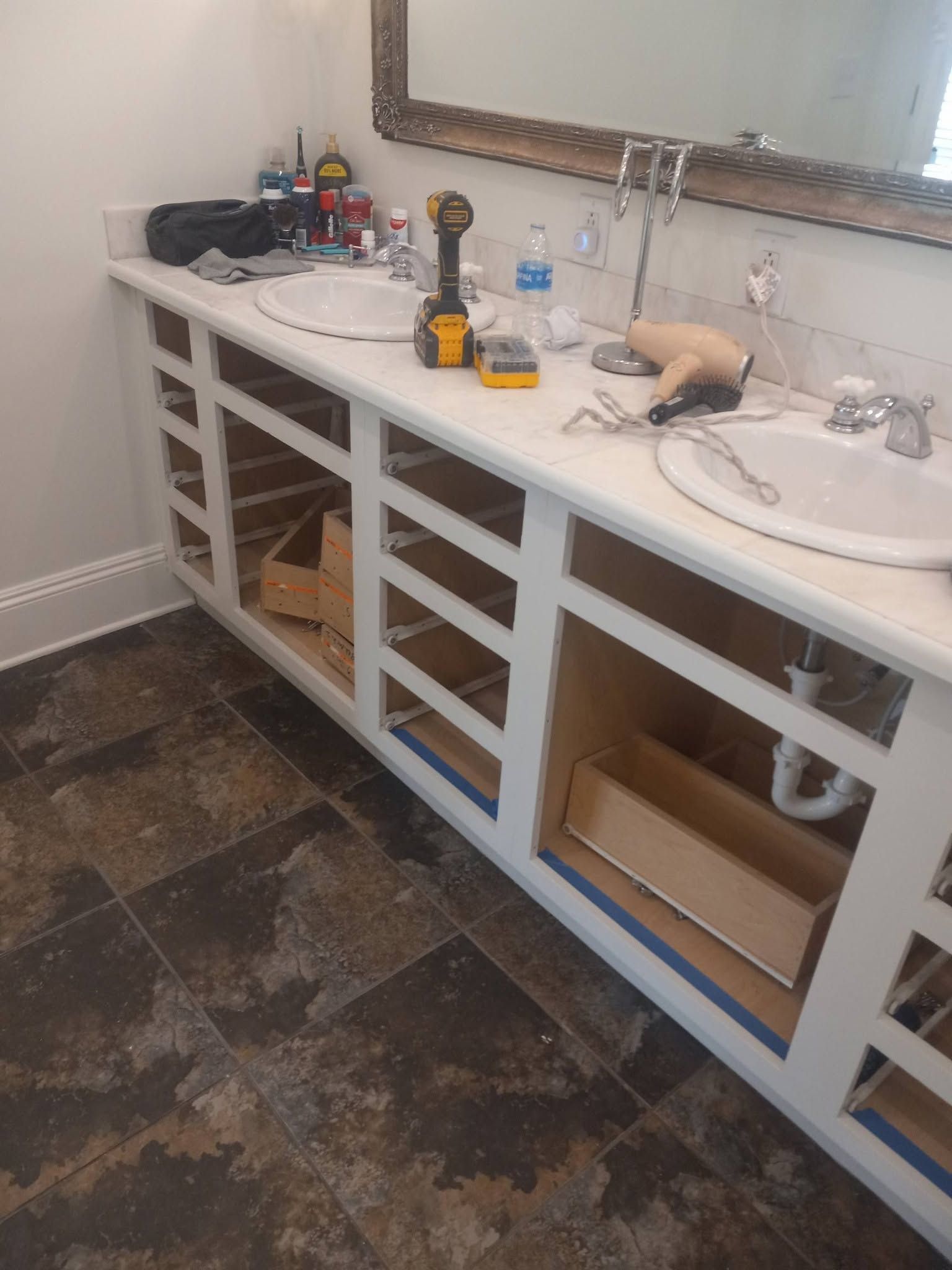 Bathroom vanity under construction with white cabinets, sink, mirror, and tools on the counter.