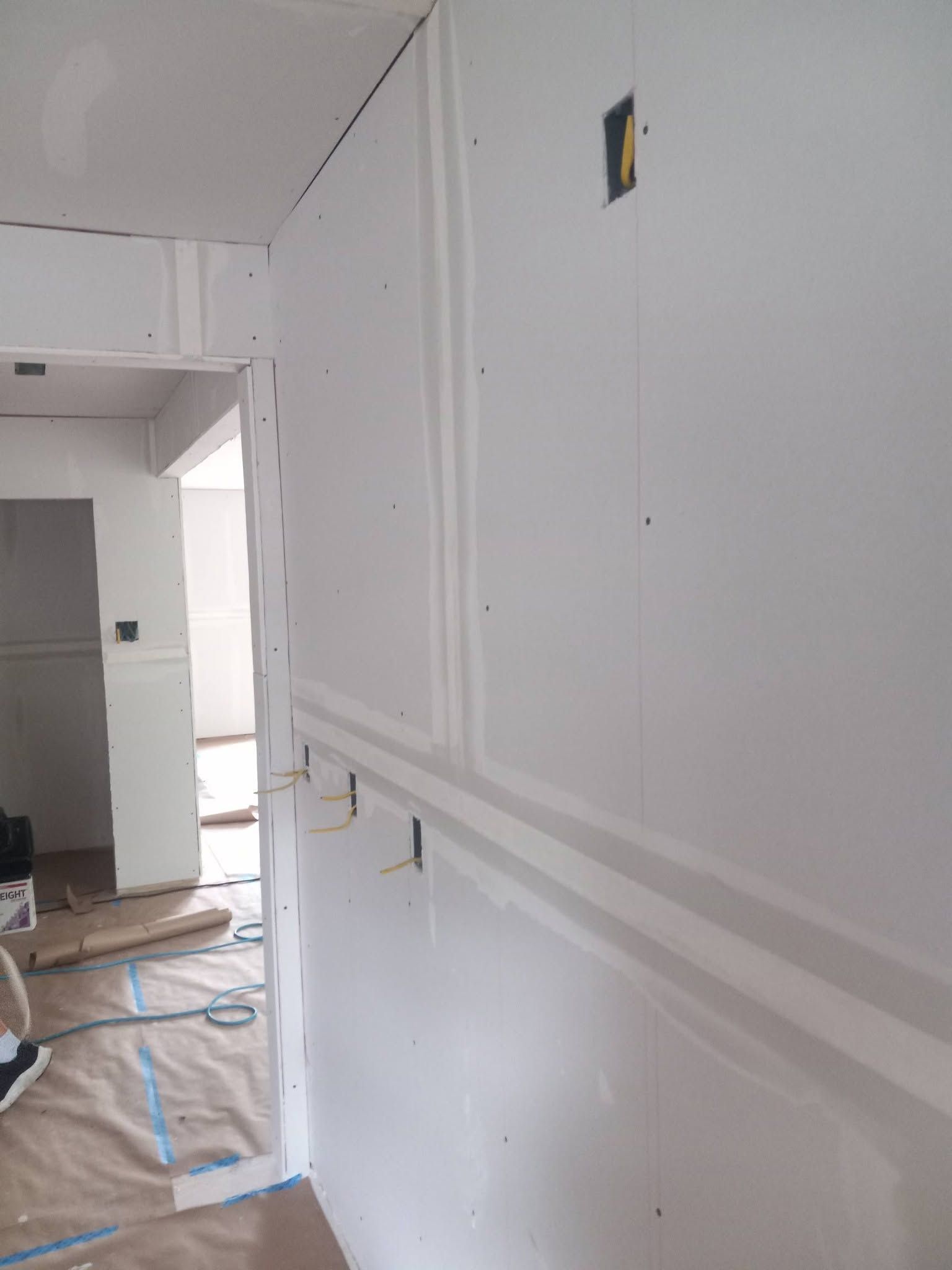 White drywall in an unfinished interior hallway with doorway opening and construction materials on floor