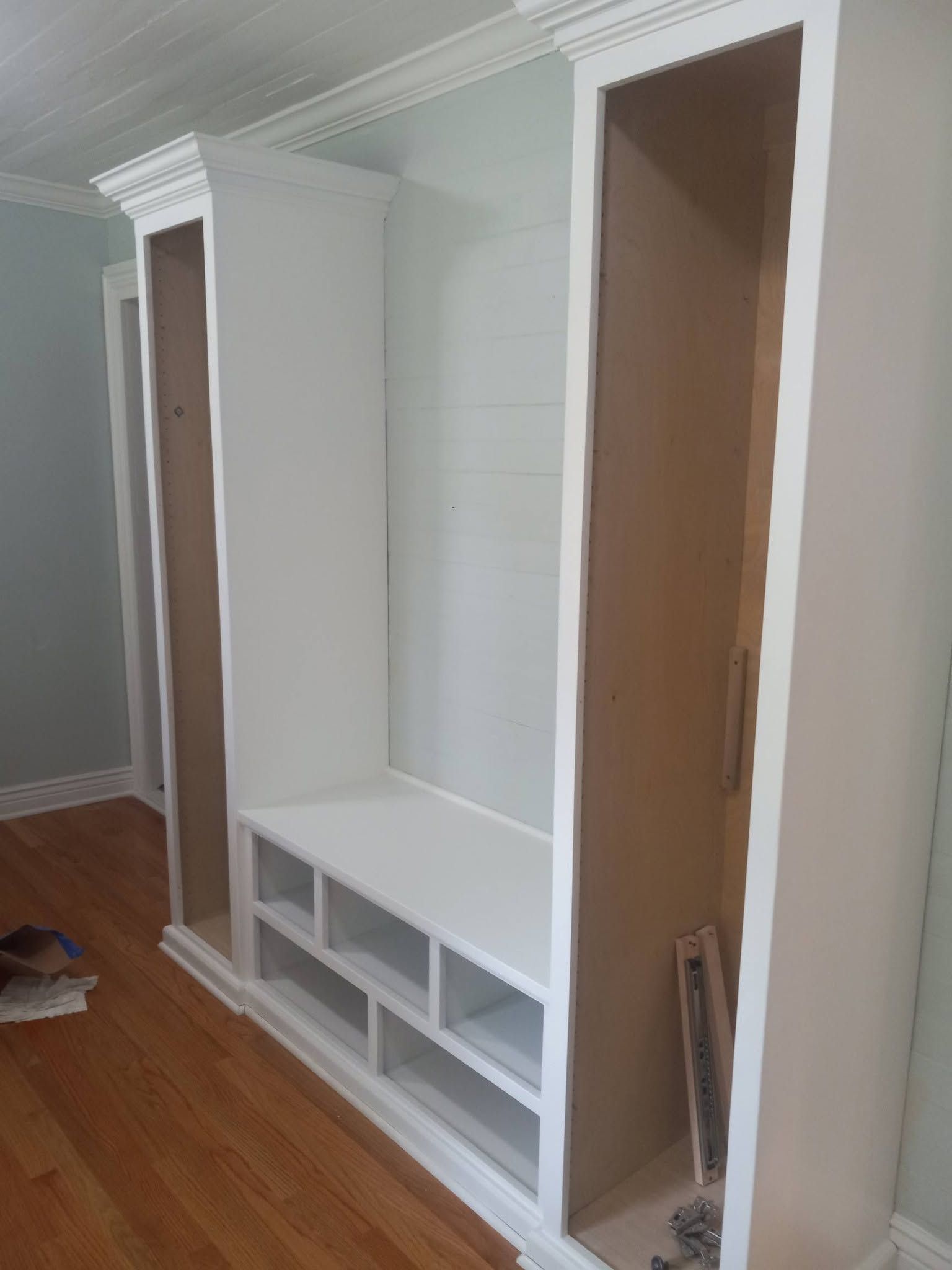 Built-in white closet with shelves and open compartments in a room with hardwood floors and gray walls
