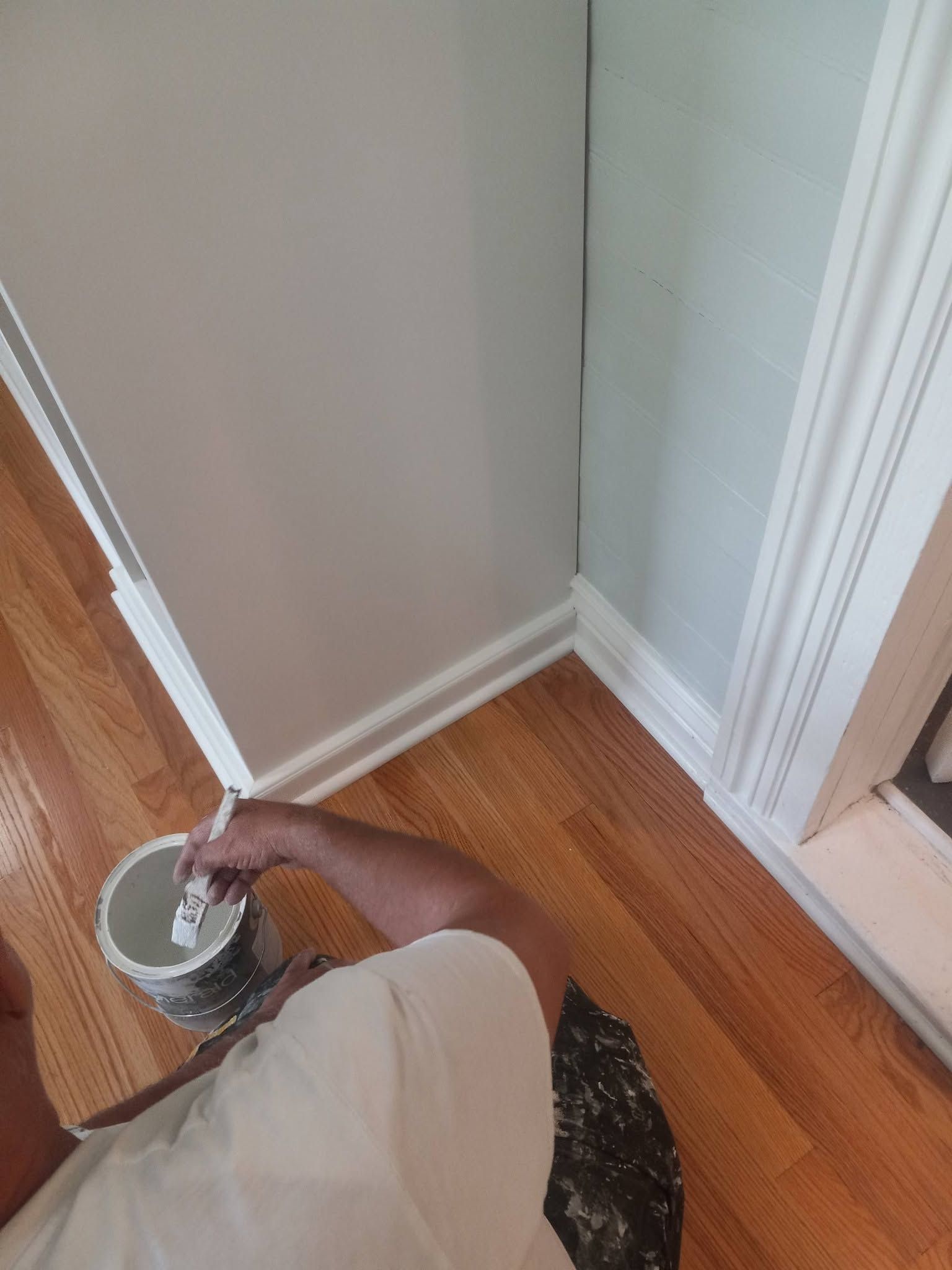 Hand brushing white trim and wall corner beside hardwood floor and doorway