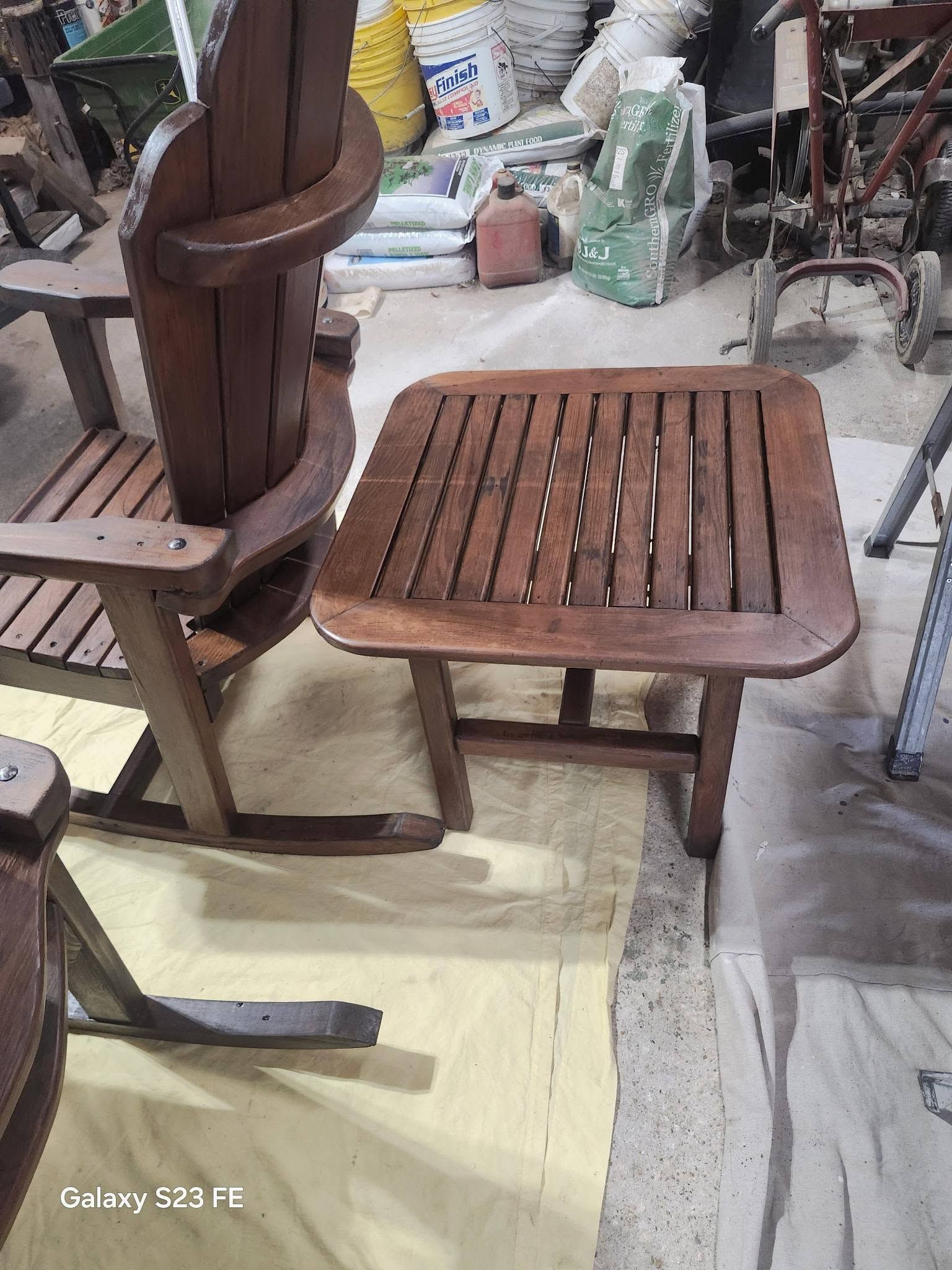 Wooden chair beside a slatted wooden side table in a cluttered indoor workshop area.