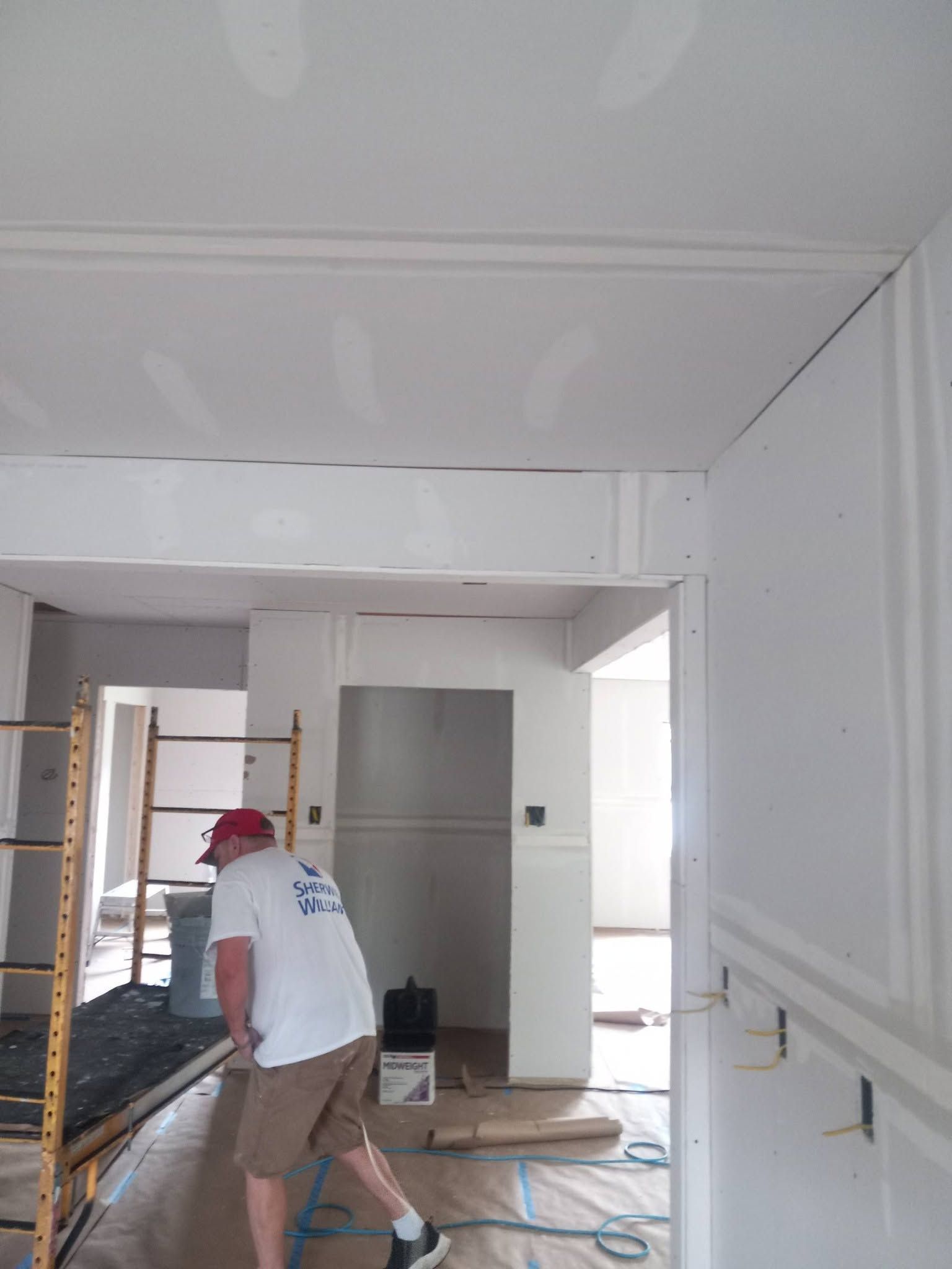 Person painting a white room with a roller near a ladder and open doorway