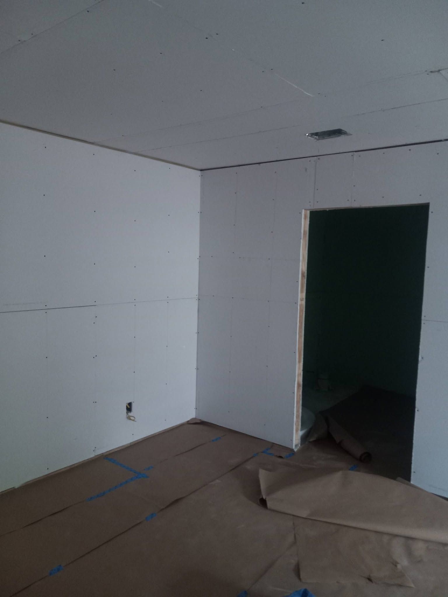 Empty unfinished room with white walls, bare floor, and a dark open doorway.