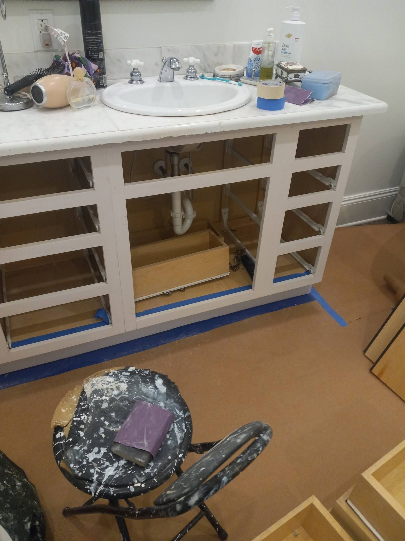 Bathroom vanity with open cabinet doors, sink, cleaning supplies, and a stool in the foreground