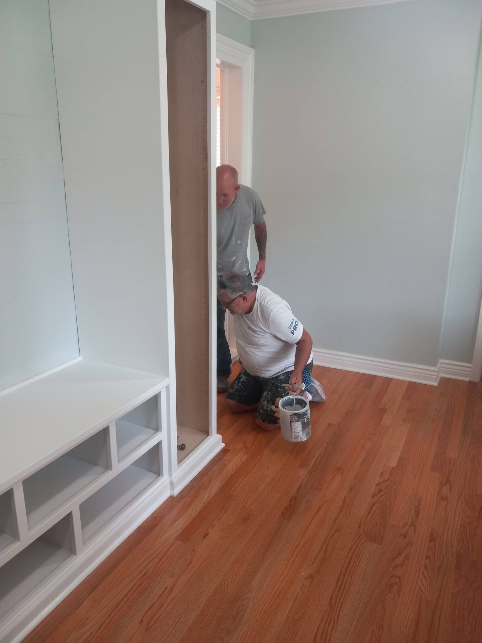 Two workers installing a white closet in a room with hardwood floors and gray walls