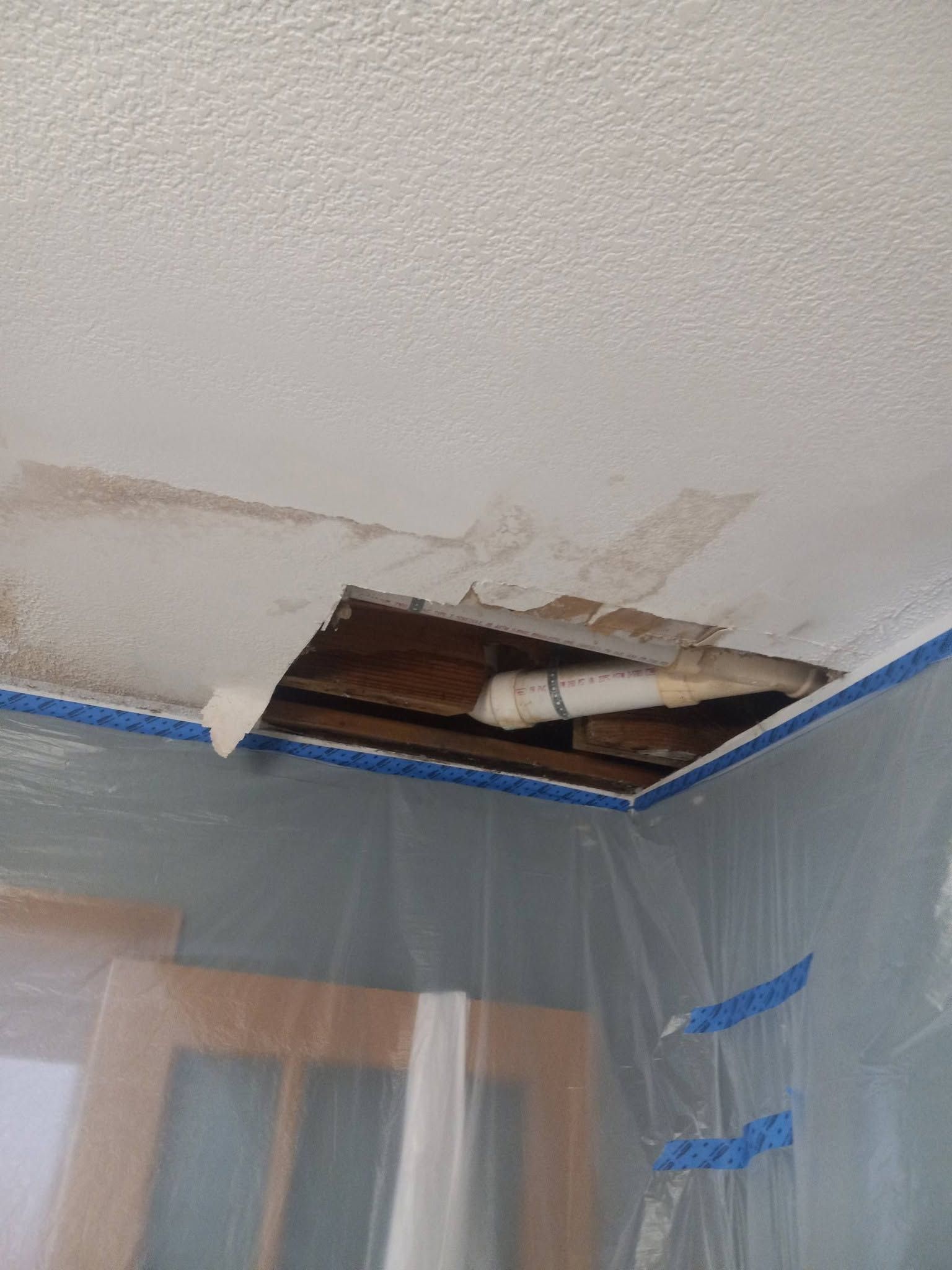 Water-damaged ceiling with peeling drywall and a torn opening above plastic-covered walls