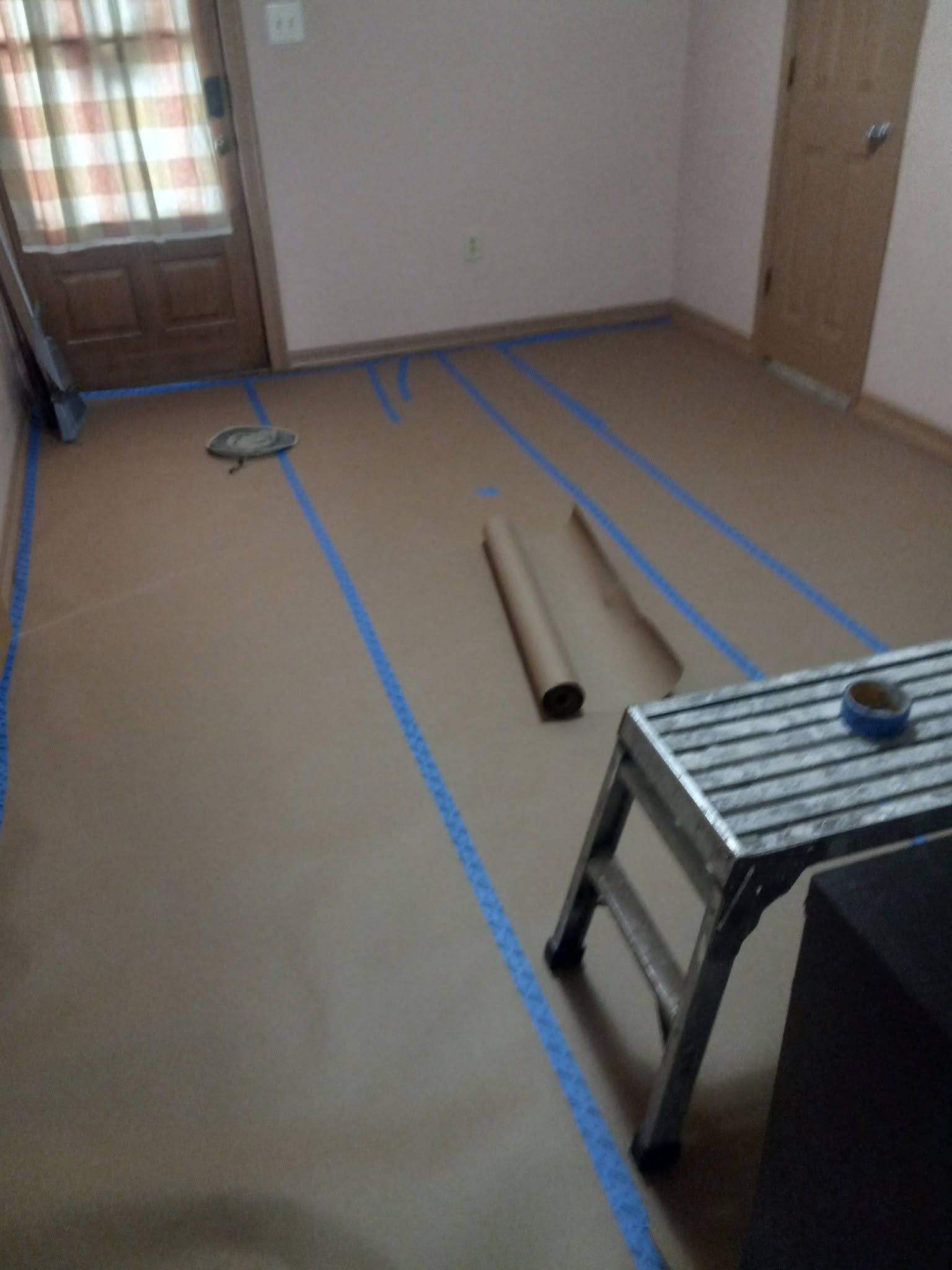 Empty room with blue tape lines on the floor, a rolled-up mat, and a small table near the camera.