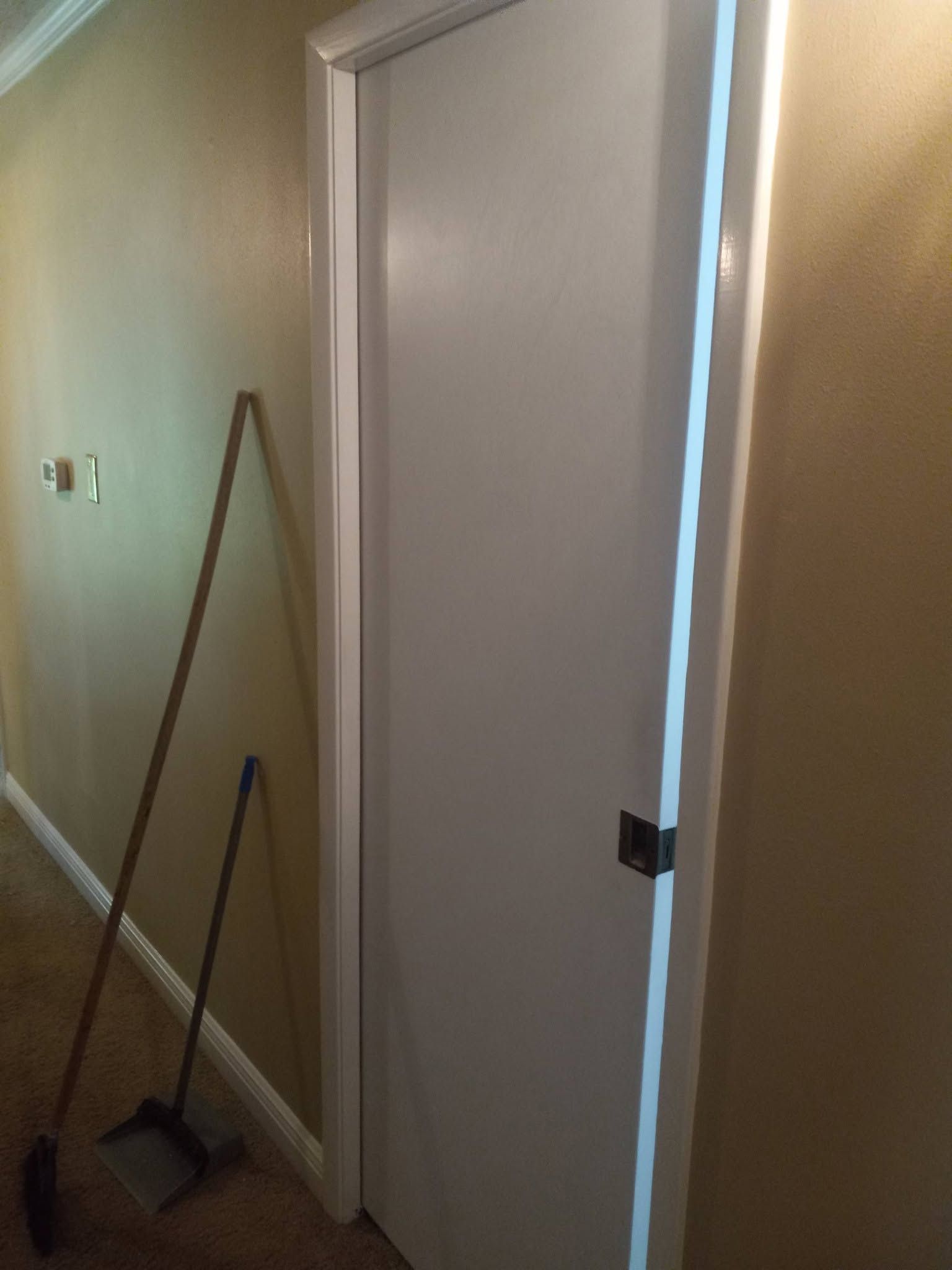 Hallway with a closed white door and a broom, dustpan, and mop leaning against the wall