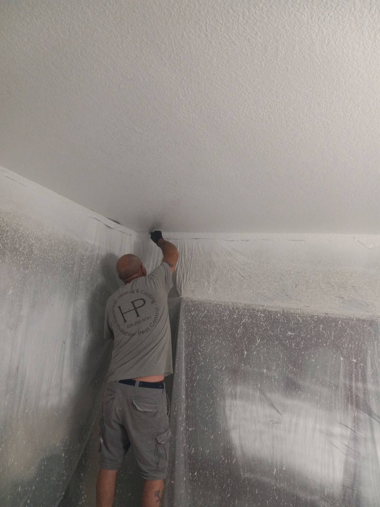 Person installing insulation in a corner of a room, reaching up to the ceiling with tools.