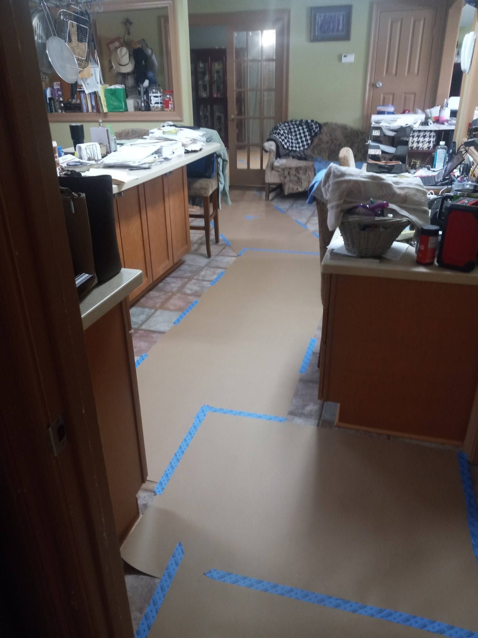Messy kitchen with countertops, cabinets, and a taped-off walkway on the floor