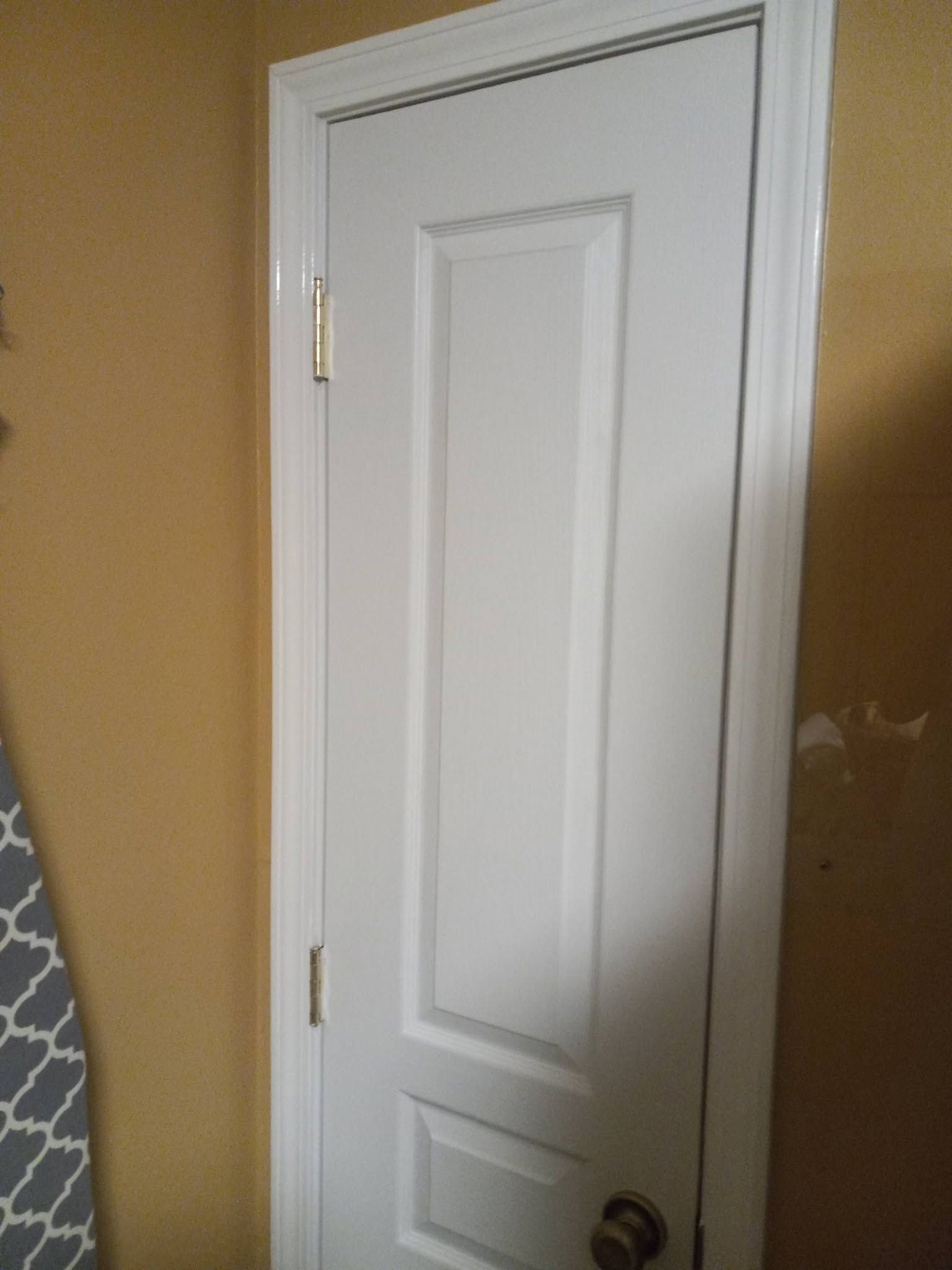 White interior door with brass hinges and dark knob in a tan-walled room.
