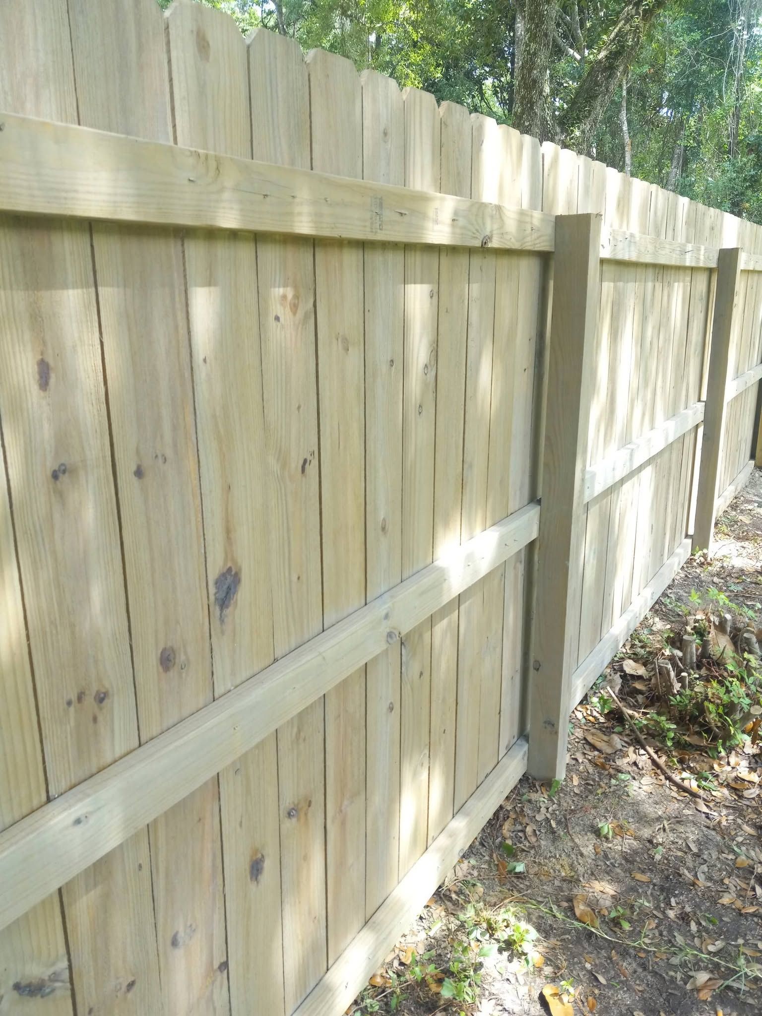 Wooden privacy fence with horizontal supports along a leafy yard edge