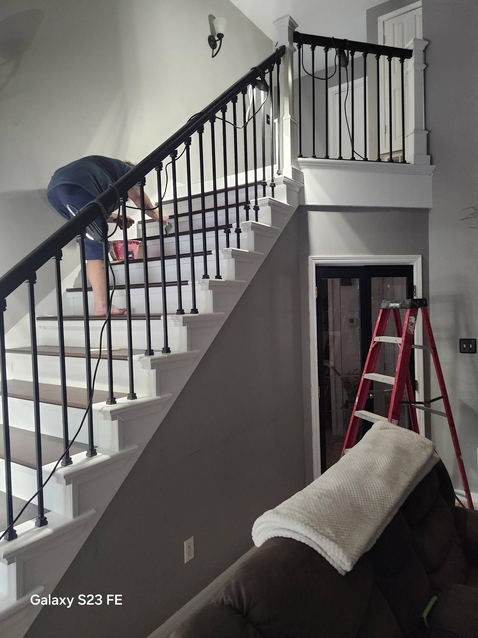 Person working on a staircase in a home, with a red ladder nearby and a couch in the foreground