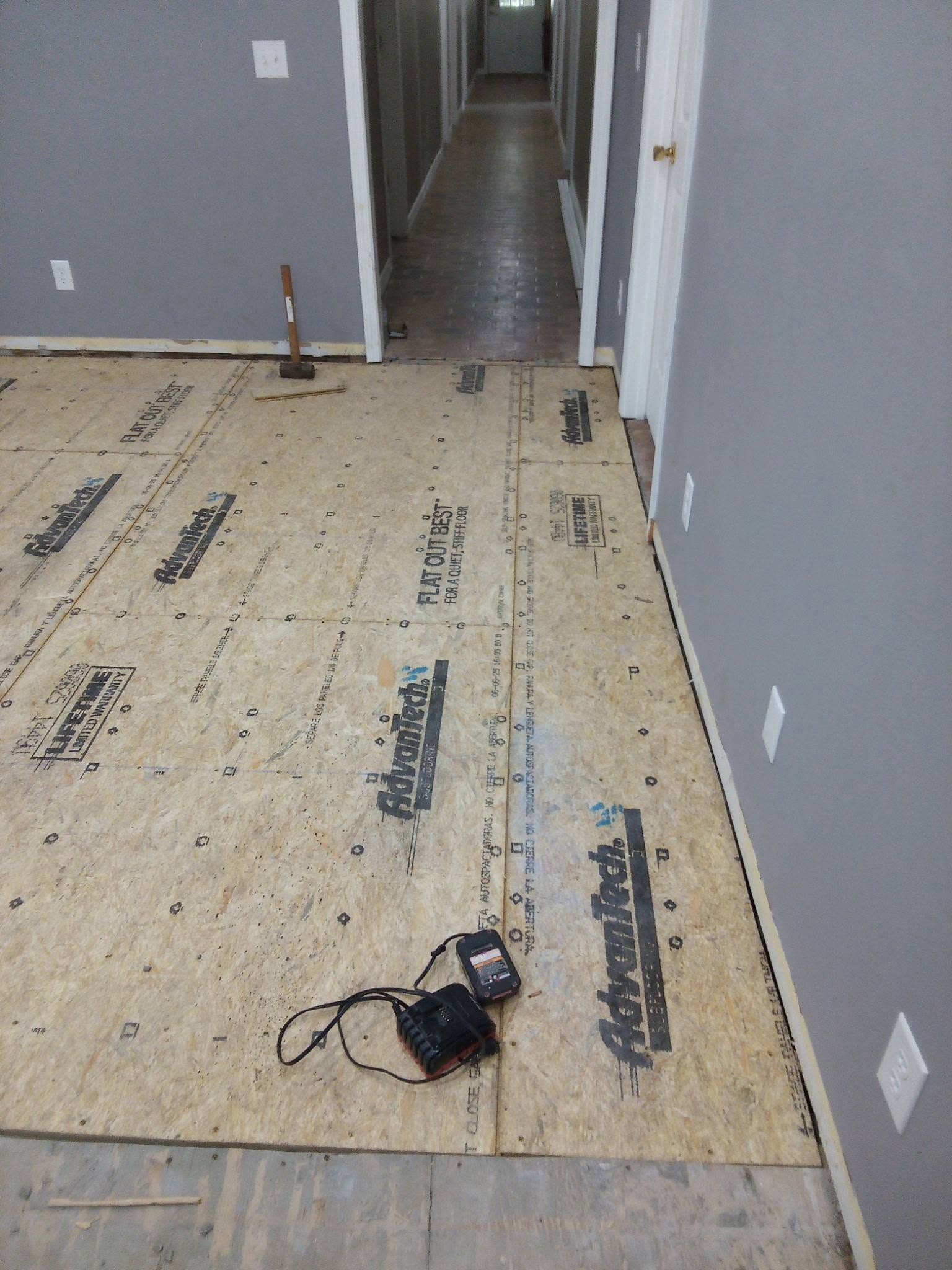 Hallway with plywood subfloor under construction, gray walls, and a power tool on the floor.
