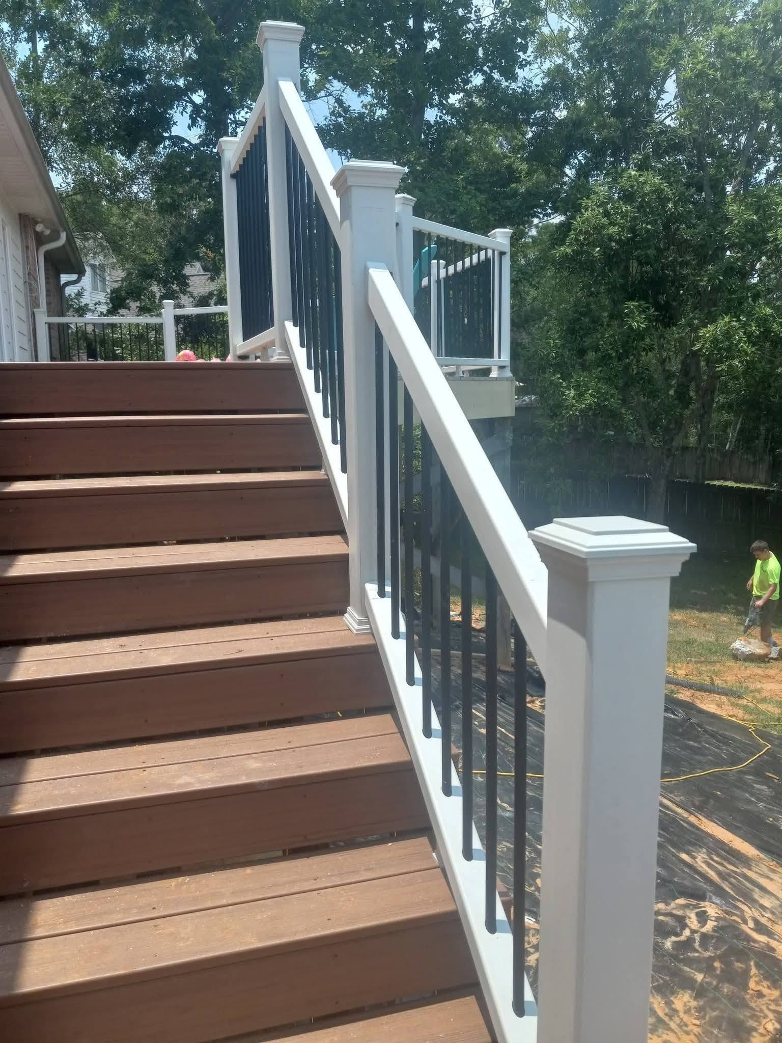 Outdoor wooden staircase with white railings and posts beside trees and a deck.